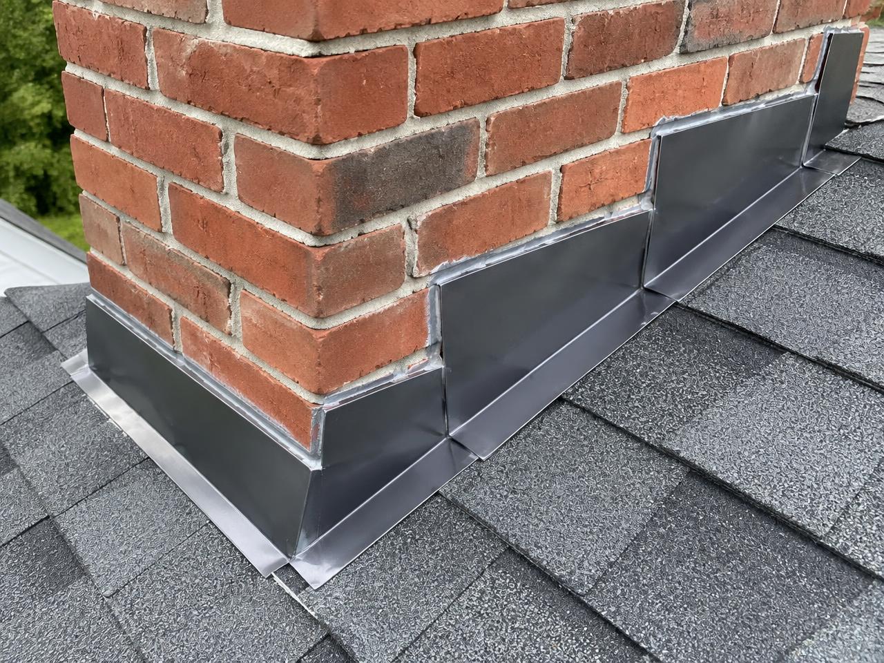 New step flashing and counterflashing cut into the mortar joints of a brick chimney on a shingle roof