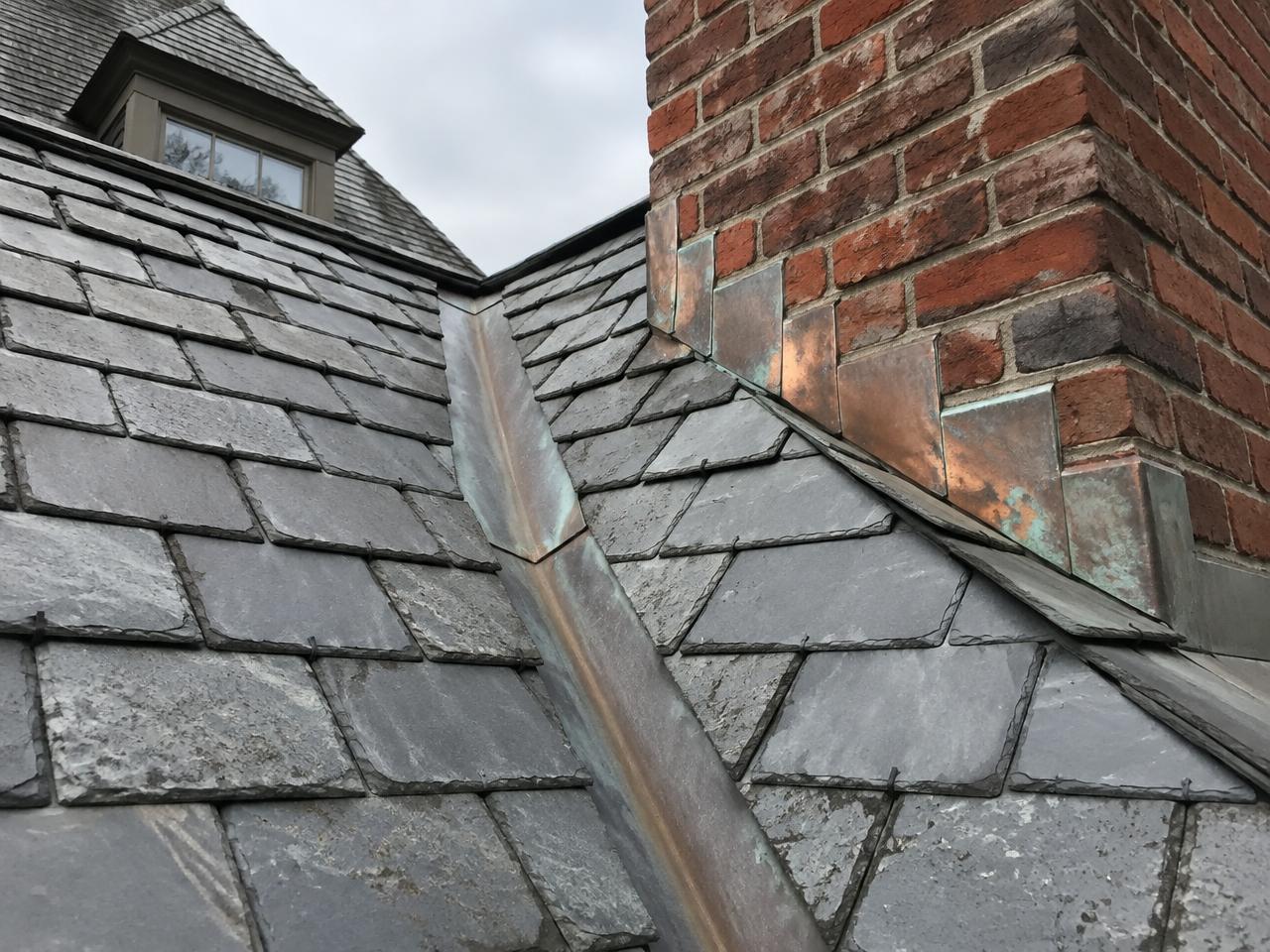 Copper-lined valley and copper step flashing against a brick chimney on a slate roof