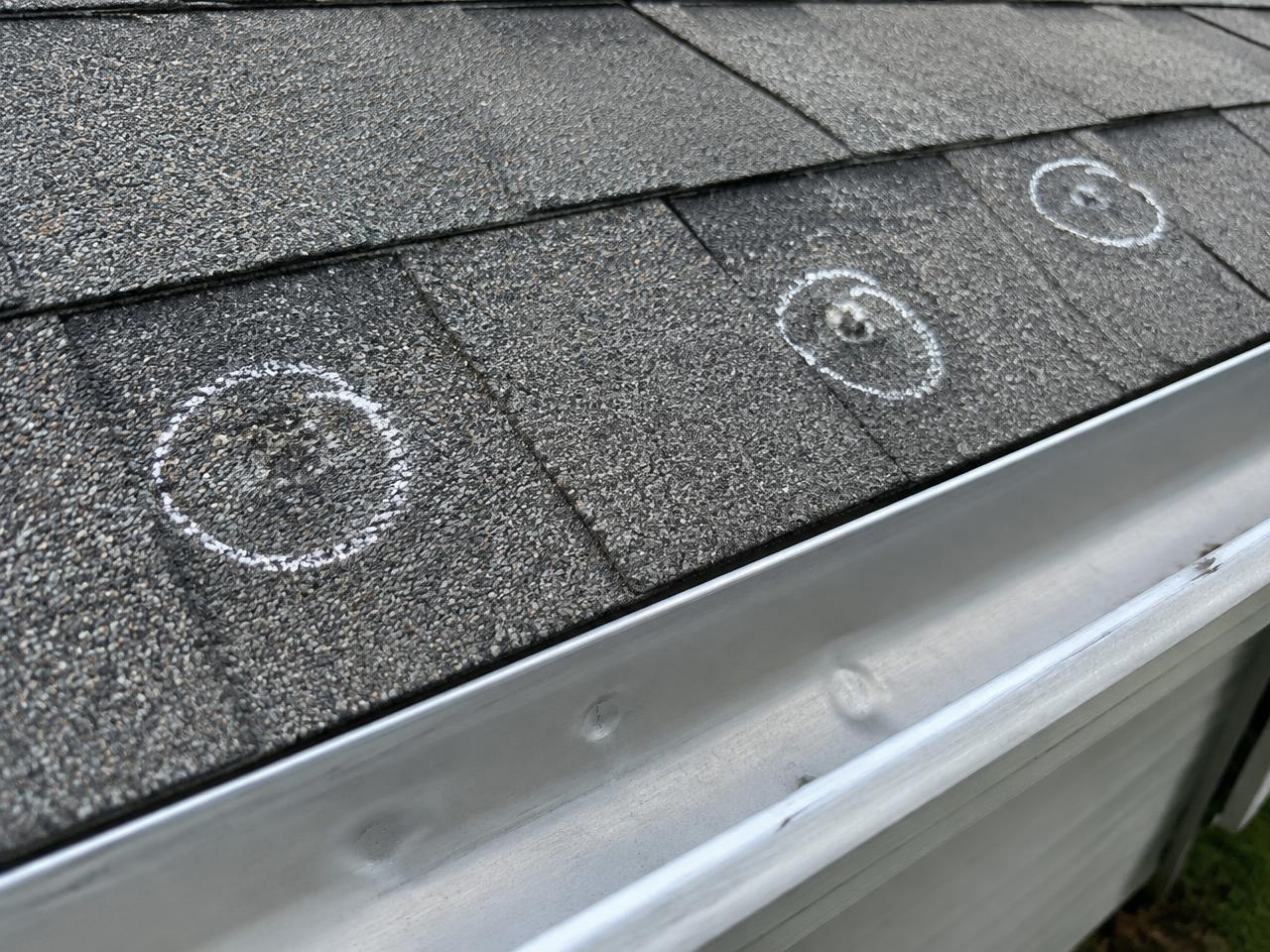 Hail dents circled in chalk on gray shingles and a dented aluminum gutter