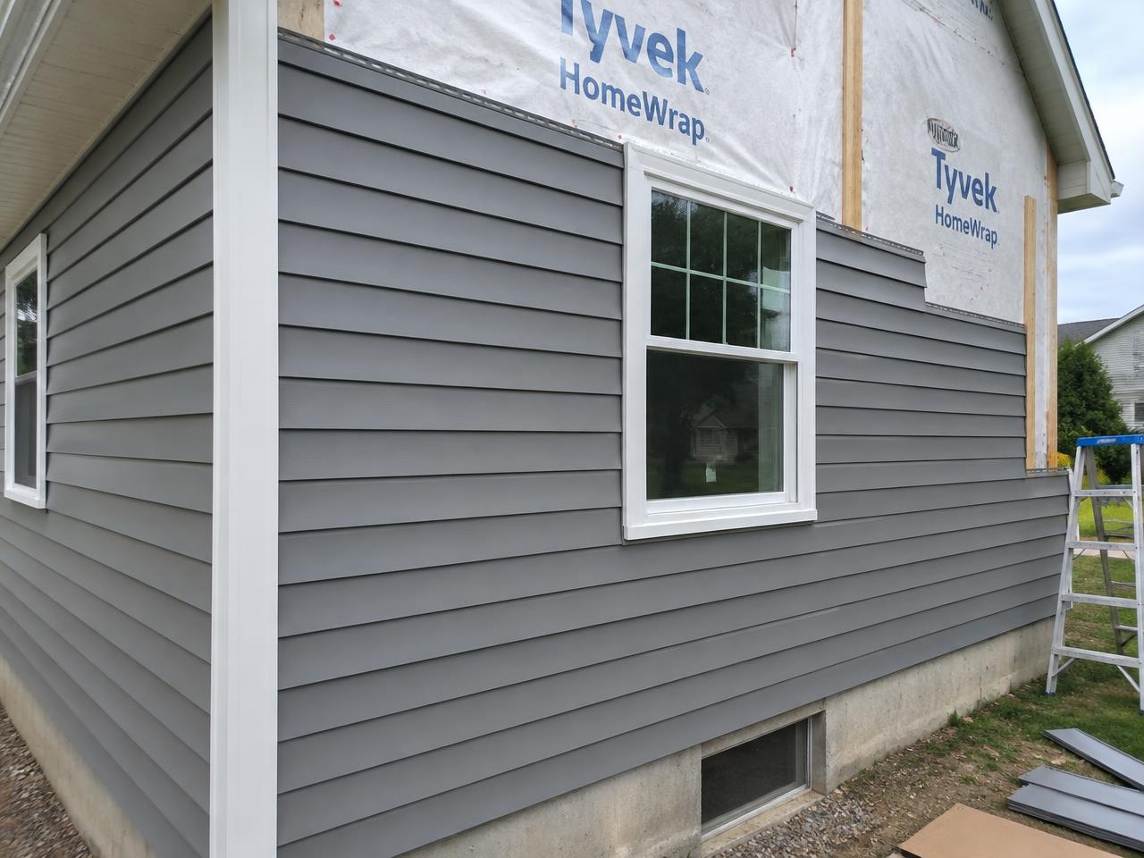 New gray vinyl siding going up on a house wall with white trim