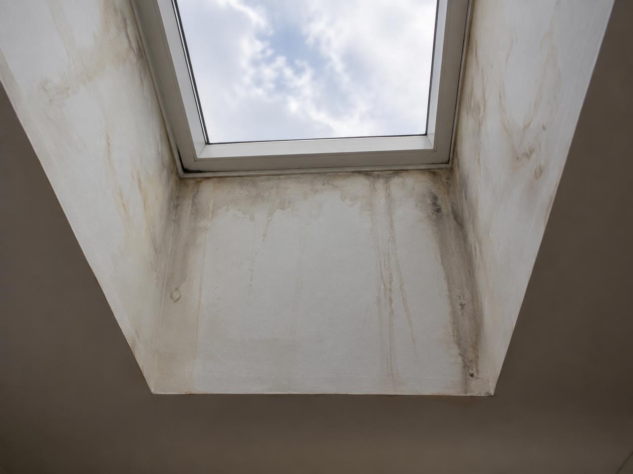 Water stains and dark streaks on the drywall around a skylight shaft