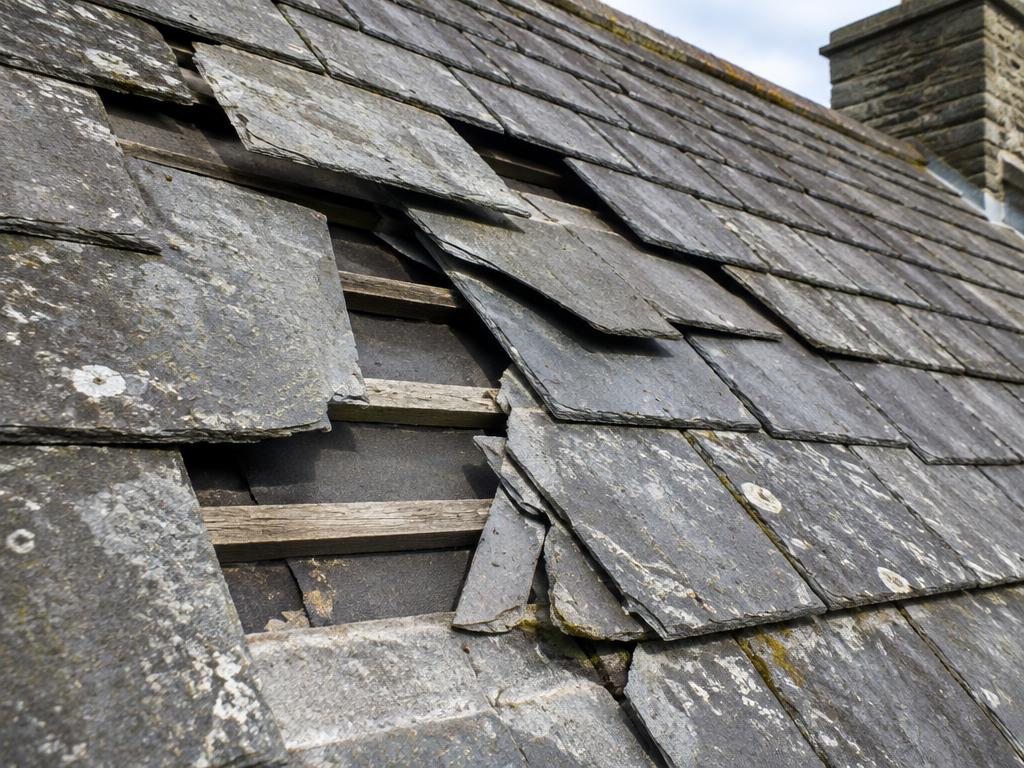 Cracked and slipped slate tiles with gaps showing the wood battens