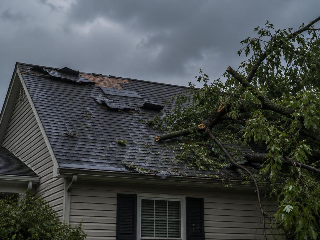 Storm damaged roof with torn shingles and fallen tree branches